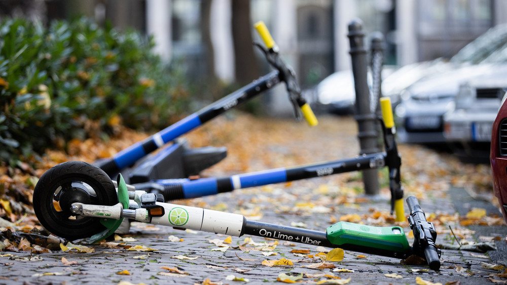 Drei E-Scooter liegen auf einem Gehweg und versperren den Weg. 