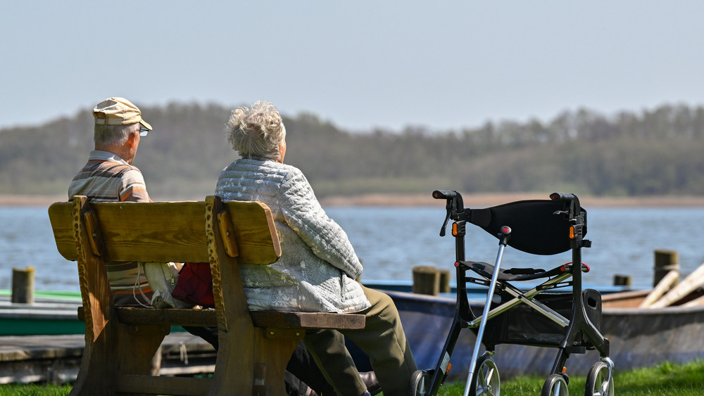 Ein älteres Paar sitzt auf einer Bank am Ufer eines Sees und genießt das sonnige Frühlingswetter.