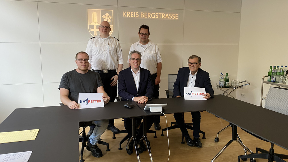 Jan Freitag (vorne links) wird selbst zum Retter, als Bernd Berg (vorne rechts) einen Herzstillstand erleidet. Die "KatRetter"-App ist seit einem Jahr erfolgreich im Kreis Bergstraße im Einsatz, erklären Landrat Christian Engelhardt (vorne, mitte), Markus Stracke (hinten links), stellv. Abteilungsleiter Gefahrenabwehr und Jörg Oberkinkhaus (hinten rechts), Fachbereichsleiter Rettungsdienst im Landkreis. 