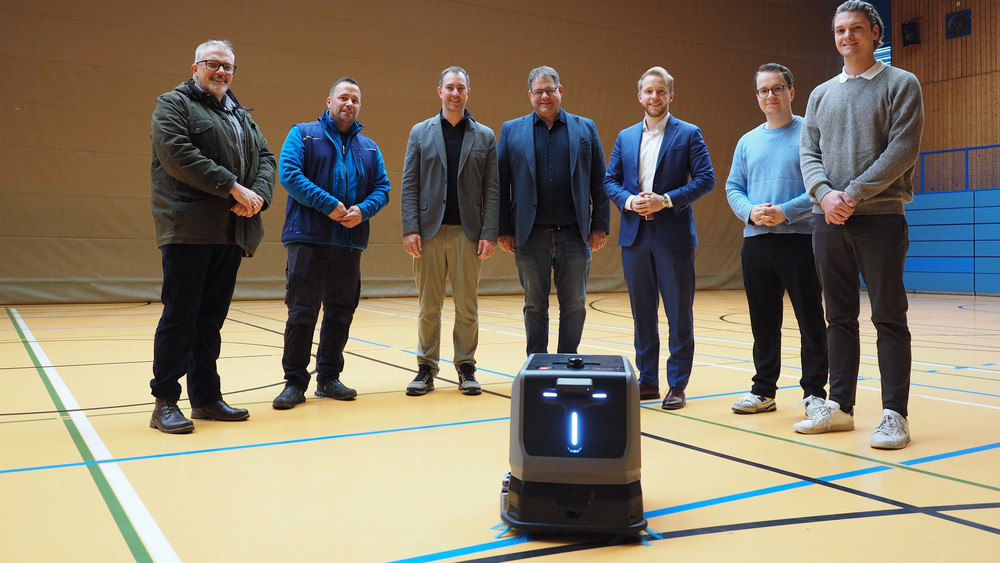 Kreisbeigeordneter Jannik Marquart (Dritter von rechts) informierte sich in der Sporthalle der Stadtschule Schlüchtern über den Einsatz des Reinigungsroboters und ließ sich von Moritz Hensel (rechts) und Carlos Seibel (Zweiter von rechts), Robots of Interest GmbH, Norman Jahn (links), Amt für Schulwesen, Bau- und Liegenschaftsverwaltung, Hausmeister Steffen Ebert (Zweiter von links), Andreas Leibold (Mitte), Leiter der Stadtschule Schlüchtern, sowie Lukas Bachmann, stellvertretender Schulleiter, Details erläutern.