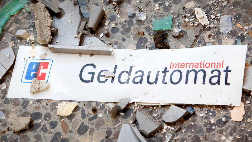 Splitter und ein Schild mit der Aufschrift «Geldautomat» liegen auf dem Fußboden vor einem gesprengten Geldautomaten.