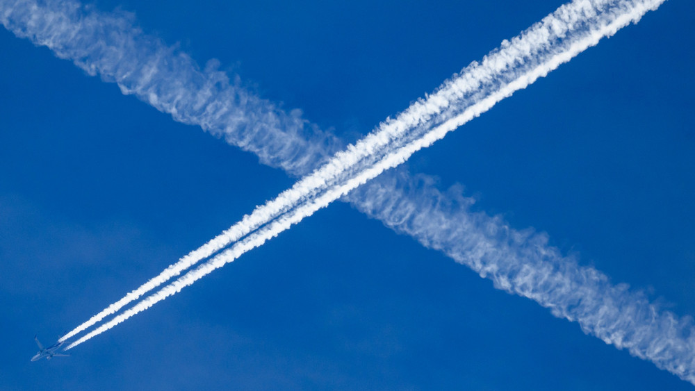 Ein Flugzeug hinterlässt Kondensstreifen am blauen Himmel.