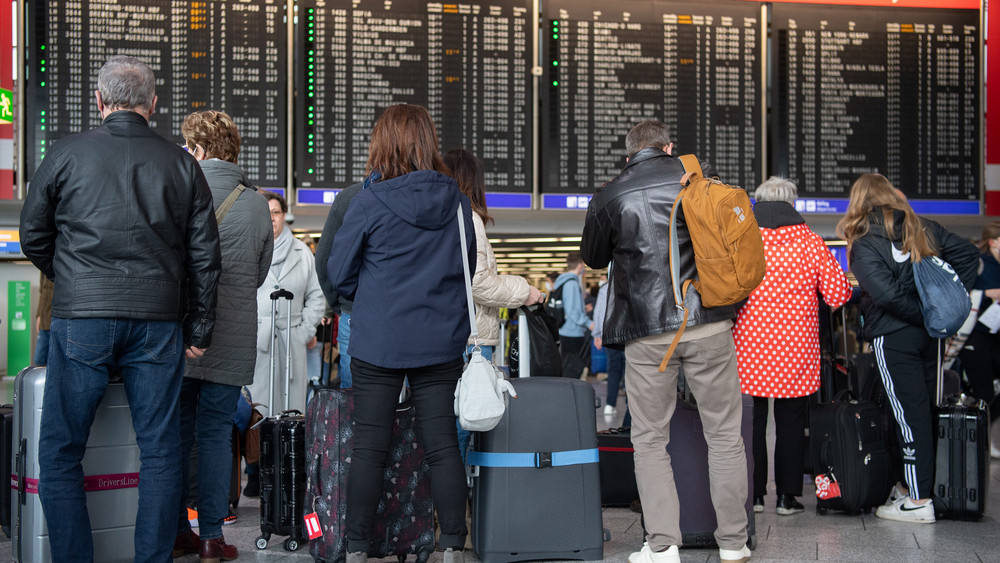 Menschen stehen am Frankfurter Flughafen vor den Infotafeln.