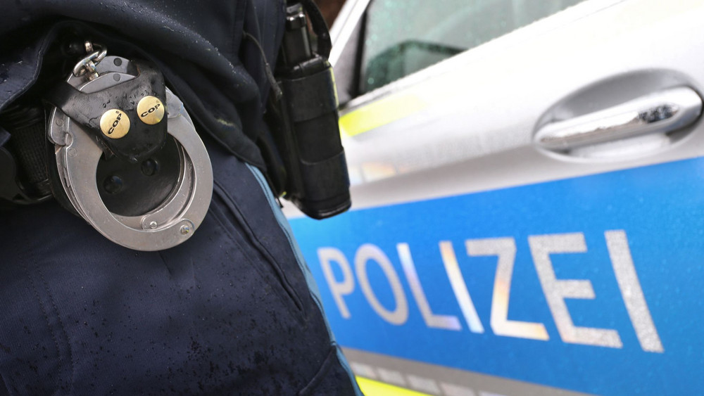 Polizist mit Handschellen vor Polizei-Auto