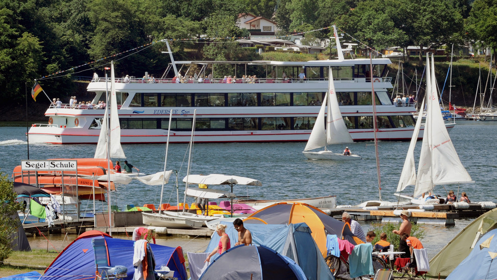 Der Campingplatz von Edertal-Rehbach am Ufer des nordhessischen Edersees mit der Halbinsel Scheid im Hintergrund und einem Ausflugsschiff dazwischen