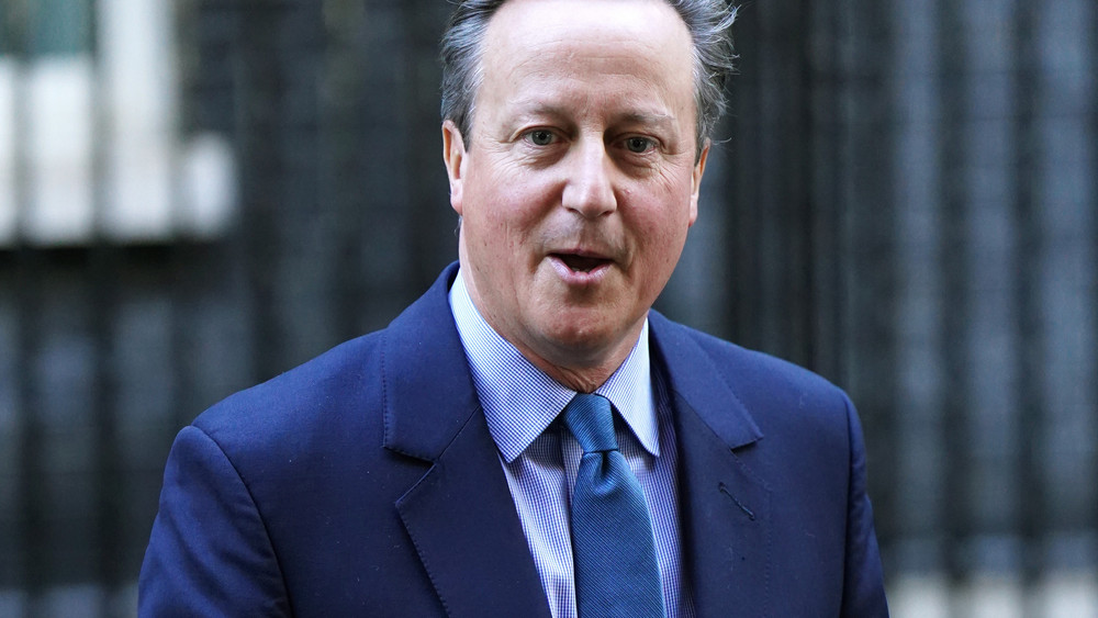 Cameron in blauem Anzug mit blauer Krawatte.