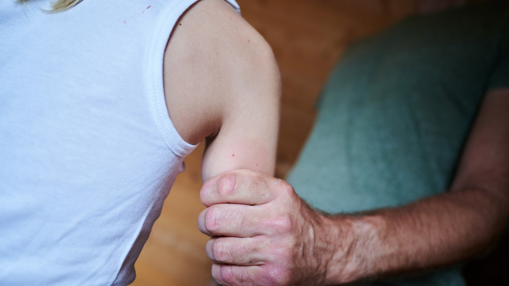 Hand eines Mannes greift fest um den Oberarm eines Kindes