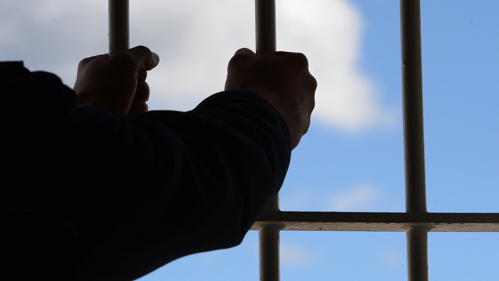 Hände am Gitterfenster eines Gefängnisses