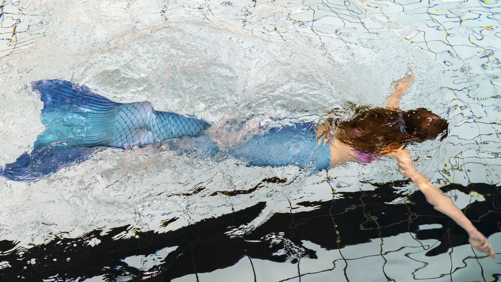 Frau mit Meerjungfrauen-Flosse schwimmt im Schwimmbad