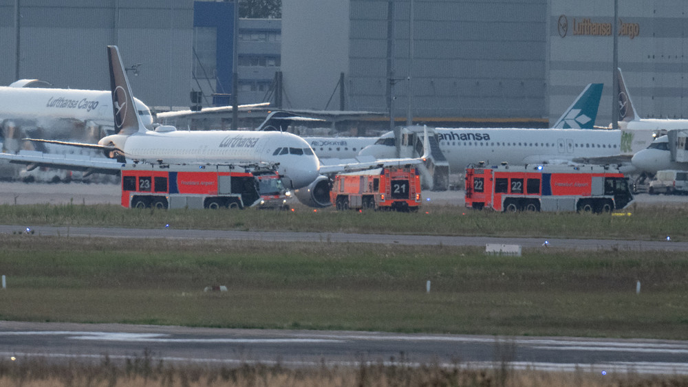 Nachdem das Flugzeug unplanmäßig zum Flughafen zurückkehren musste, stehen Feuerwehrfahrzeuge an dem gelandeten Airbus der Lufthansa.