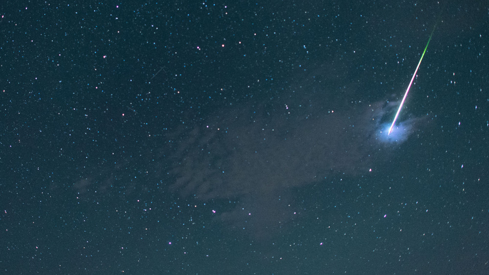 Eine helle Sternschnuppe ist am dunklen Himmel zu sehen. 