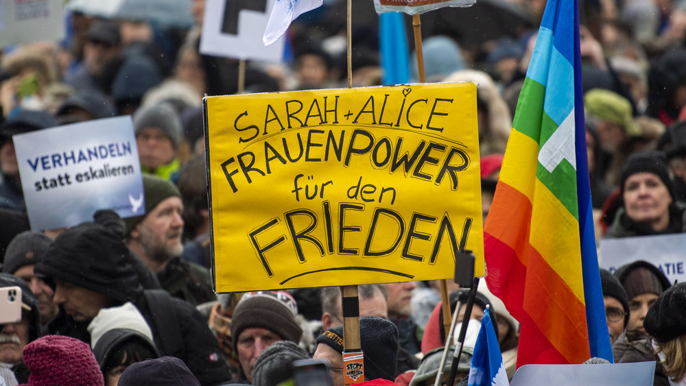 Ein Teilnehmer einer Demonstration für Verhandlungen mit Russland am Brandenburger Tor hält ein Plakat mit der Aufschrift «Sarah + Alice - Frauenpower für den Frieden».