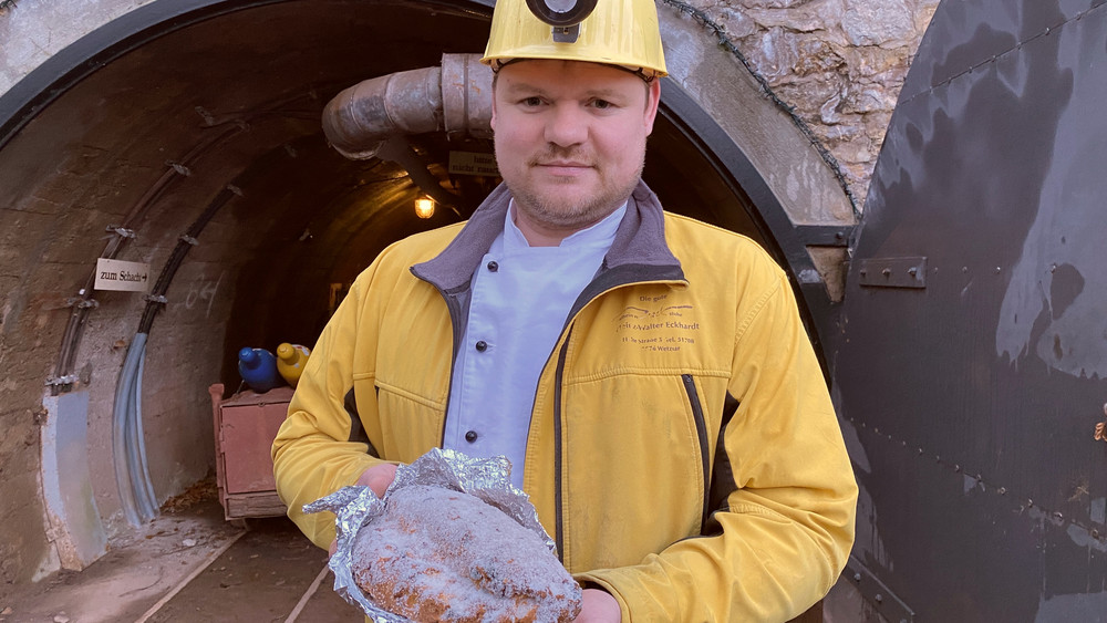 Der Bäcker mit Schutzhelm präsentiert vor dem Bergwerksstollen seinen Christstollen