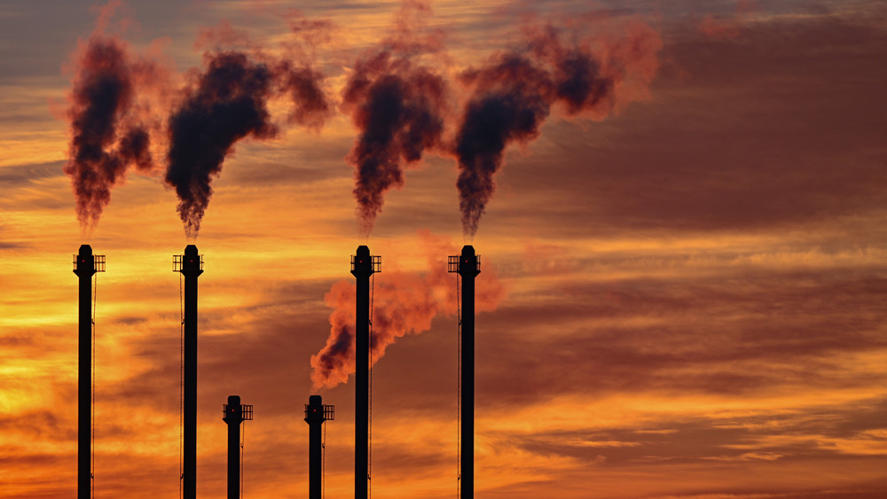 Im Sonnenuntergang steigt Rauch aus den Schornsteinen eines Blockheizkraftwerkes.  Die Emissionen im Energiesektor stiegen deutlich an.