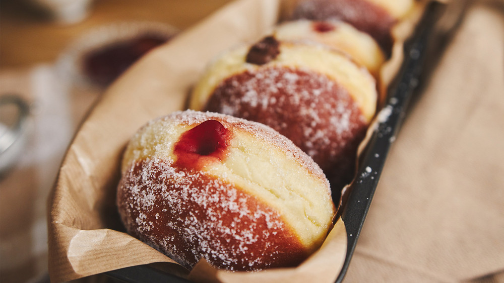 Eine Reihe von Kreppel in Backpapier liegen mit der Marmeladenöffnung nach oben.