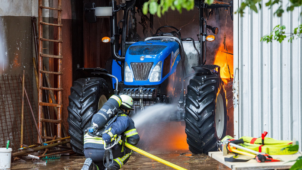 Feuerwehrmann löscht einen Traktor in der brennenden Scheune.