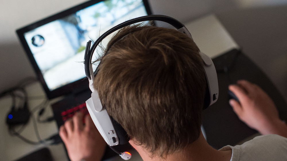 Ein Jugendlicher sitzt mit einem Headset vor einem Laptop und spielt ein Online-Computerspiel