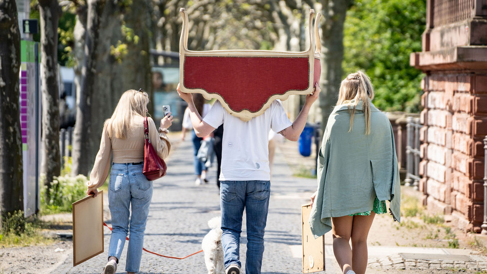 Flohmärkte in Hessen: ein Mann trägt ein Möbelstück auf den Schultern, zwei Frauen tragen Bilderrahmen