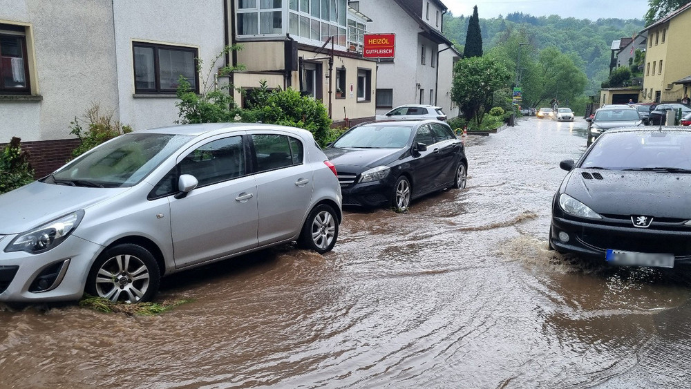 Autos fahren in Schriesheim-Altenbach über eine überflutete Sraße.