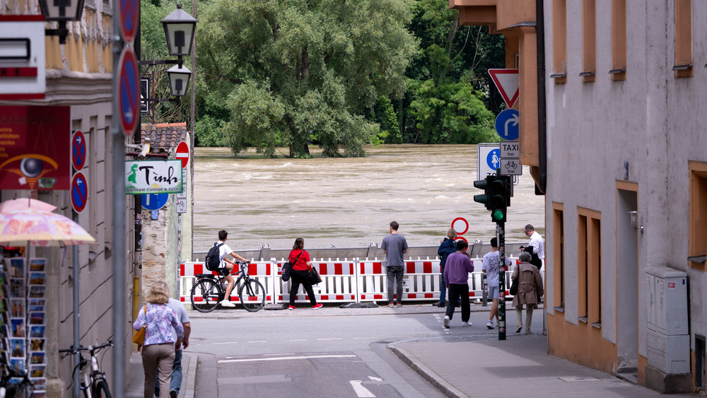 Passanten schauen sich in der Regensburger Altstadt am Donauufer hinter einer Schutzwand das Hochwasser an. Seit Tagen kämpfen die Helfer in Bayern gegen die Flut und ihre Folgen.