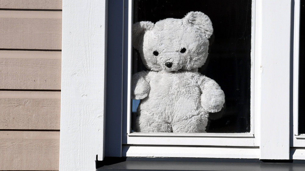 Ein Teddybär steht an ein Fenster gelehnt