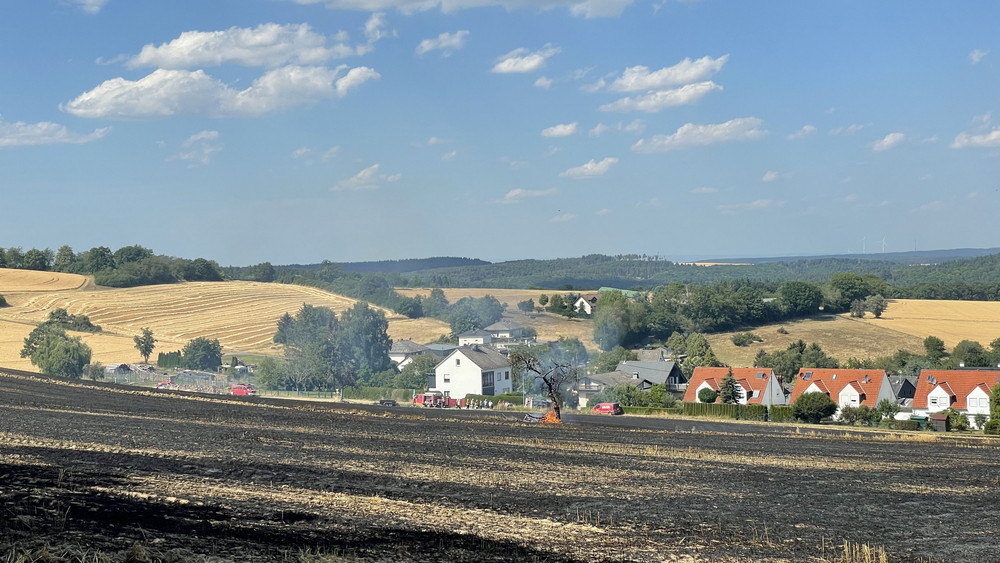 Die Feuerwehr löscht einen Flächenbrand bei Bad Schwalbach kurz bevor die Flammen eine Reihe Wohnhäuser erreichen.