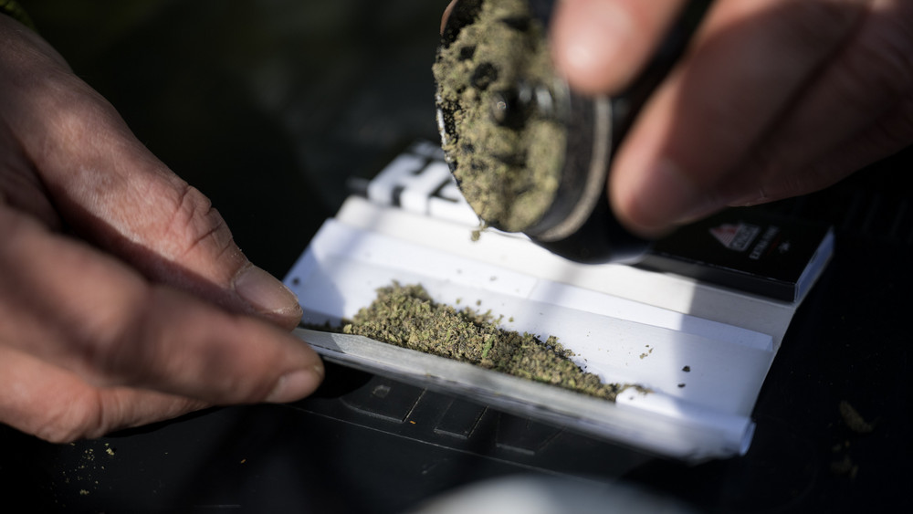 Ein Mann schüttet zerkleinertes Marihuana in einen Joint.