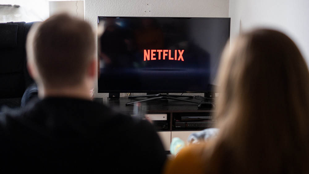 Ein Paar sitzt vor dem Fernseher, auf dem das Netflix-Logo zu sehen ist. 