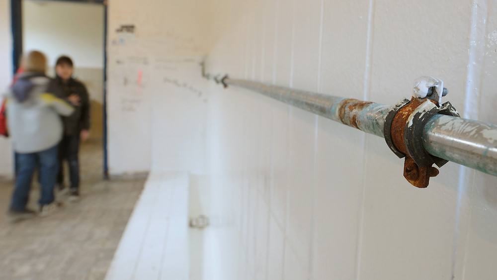 In einer Toilette an einer Schule ist ein verrostetes Rohr zu sehen.