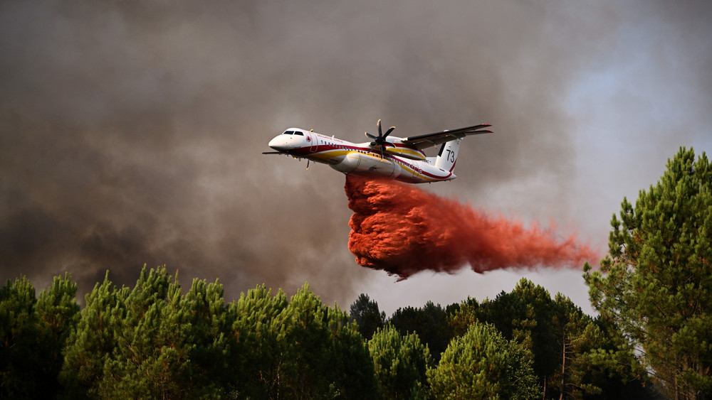 Eine De Havilland Canada Dash 8-400 versprüht Löschmittel, während sie bei den Waldbränden im Südwesten Frankreichs über einen Wald fliegt.