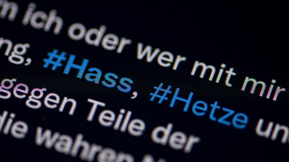 Auf dem Bildschirm eines Smartphones sieht man die Hashtags (#) Hass und Hetze in einem X-Post.