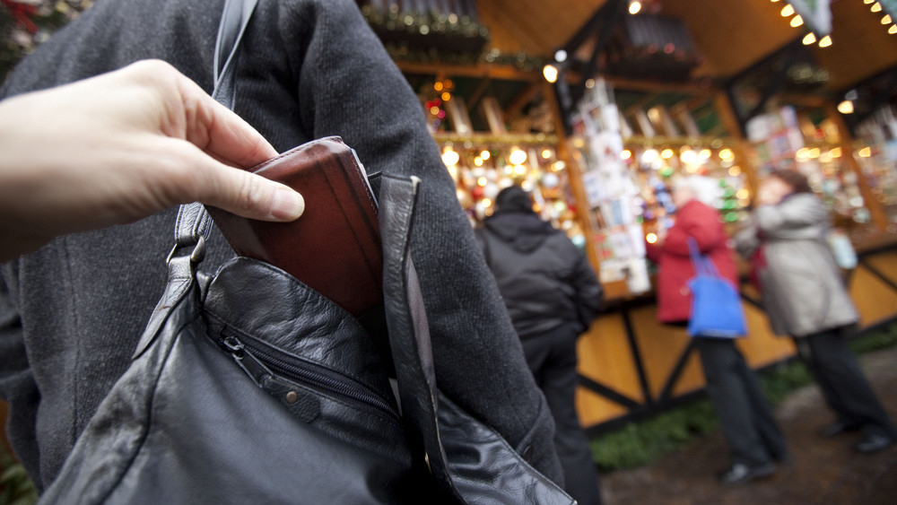 Ein Mann zieht auf diesem gestellten Bild auf einem Weihnachtsmarkt einer Besucherin die Geldbörse aus der Handtasche.