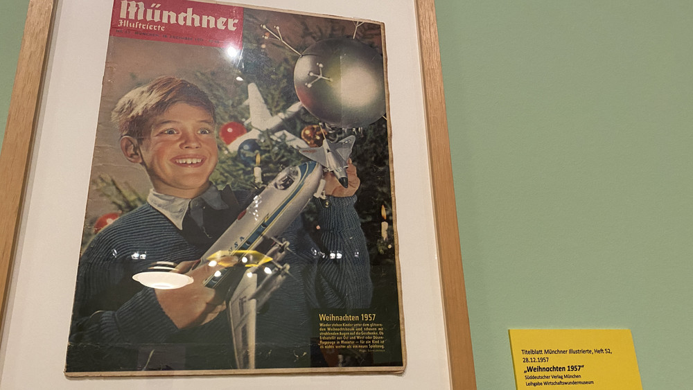 Auf dem Bild zu erkennen: Ein Junge mit strahlenden Augen - in seinen Händen hält er einen Sputnik und ein Düsenflugzeug.