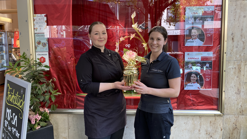 Lisa und Annika stehen vor dem Cafe Geißner und halten den goldenen Cupcake.