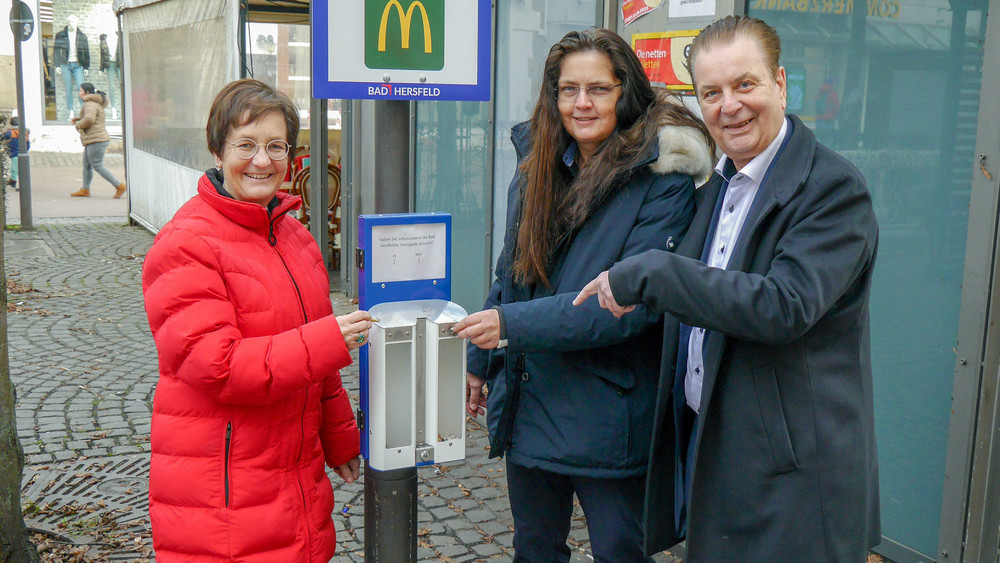 Bürgermeisterin Anke Hofmann an einem der drei Kippster. In einem Rahmen über den Aschenbechern stellt die Stadt eine Frage - darunter wählt man per Kippen-Einwurf die Antwort.