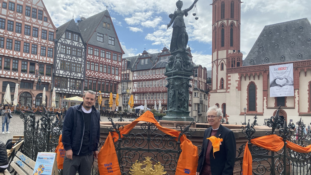 Zum Welt-MS-Tag am 30.Mai schmückt Eintracht Frankfurt Legende Alex Maier (links) zusammen mit dem Geschäftsführer der Deutschen Gesellschaft für Multiple Sklerose Hessen Benno Rehn (rechts) den Gerechtigkeitsbrunnen auf dem Römerberg.