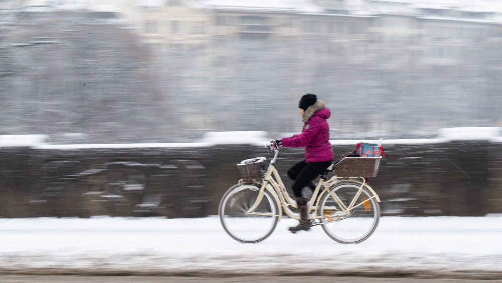 Eine Frau fährt auf ihrem Fahrrad über eine verschneite Straße