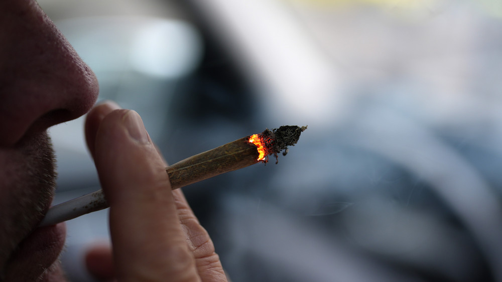Ein Mann raucht während der Autofahrt am Steuer einen Joint.