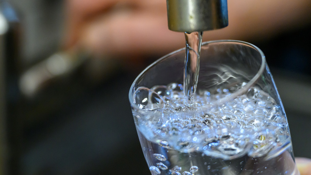 Wasser läuft aus Hahn in Glas Symbolbild