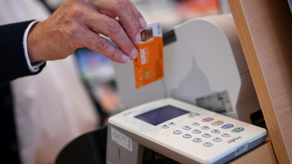Eine Person legt die Gesundheitskarte eines Patienten in ein Kartenlesegerät in einer Apotheke.
