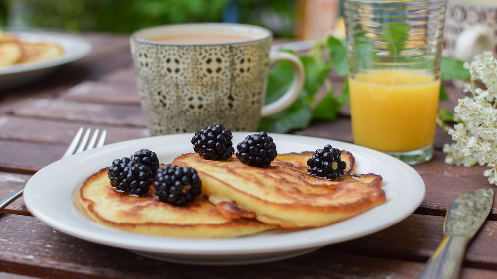 Frische Pancakes mit Beeren neben einem Glas Orangensaft