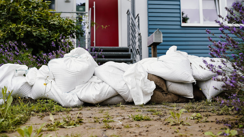 Sandsäcke liegen vor einem Haus, das vom Hochwasser betroffen ist