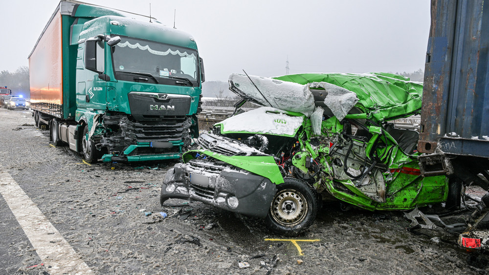 Ein kaputtes, grünes Auto. Dahinter ein Lkw.