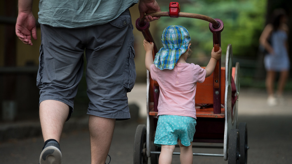 Vater geht mit Kind und Kinderwagen spazieren.