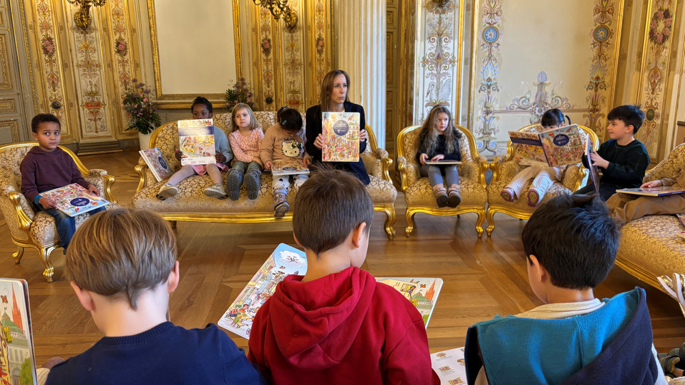 Landtagspräsidentin Wallmann schaut das neue Landtags-Wimmelbuch zusammen mit Vorschulkindern an.