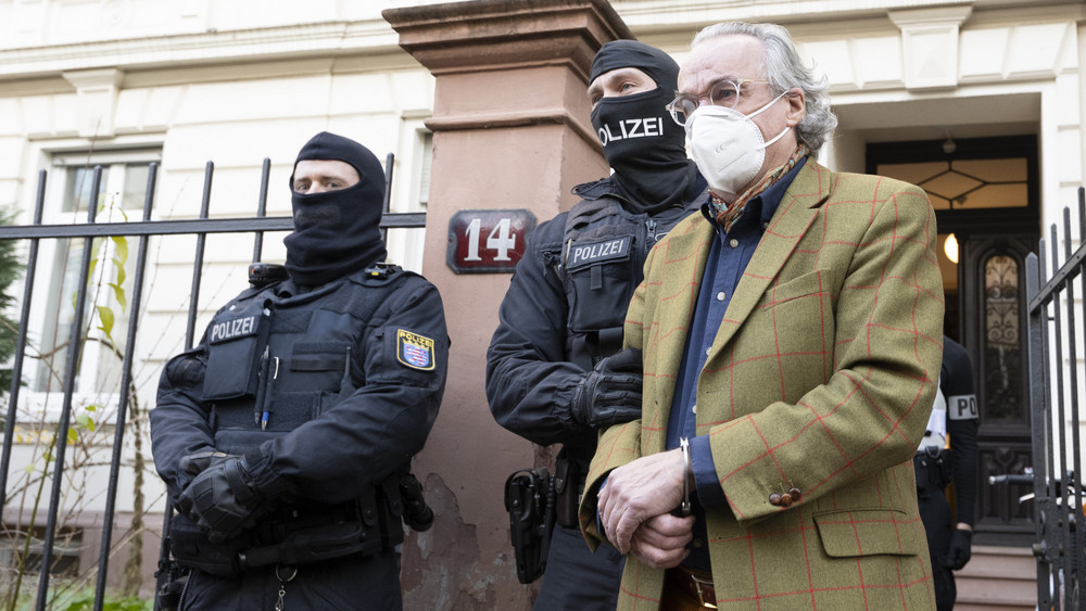 Bei einer Razzia gegen sogenannte «Reichsbürger» im Dezember 2022 haben vermummte Polizisten nach der Durchsuchung eines Hauses Heinrich XIII Prinz Reuß (r) zu einem Polizeifahrzeug geführt. Der Prozess gegen ihn und acht weitere Angeklagte in Frankfurt soll nun am 21. Mai beginnen, teilte das Gericht mit.