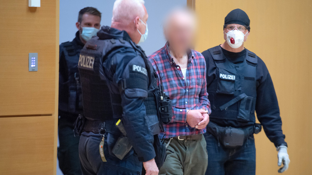 Der angeklagte Vater des Hanau-Attentäters wird von einem Polizisten in den Verhandlungssaal geführt.