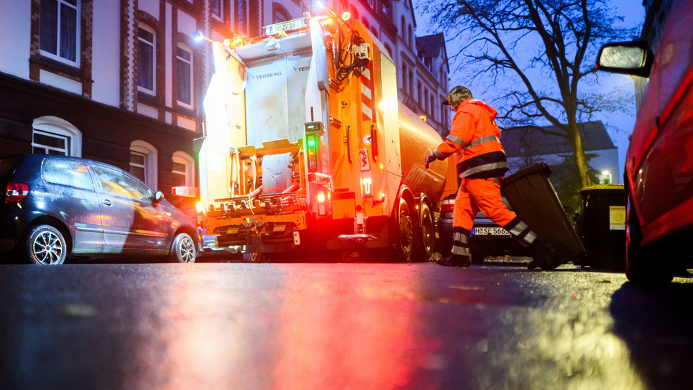 Mann entleert Mülltonne in Müllfahrzeug.