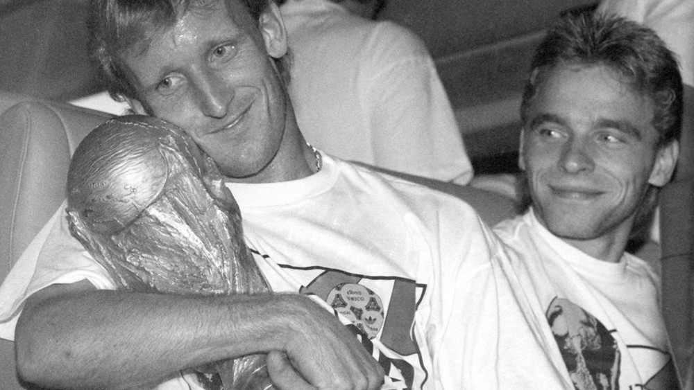 Der deutsche Abwehrspieler Andreas Brehme (l) hält 1990 in Rom den eroberten WM-Pokal im Arm und sein Teamgefährte Thomas Häßler schaut lächelnd zu (Archivbild vom 09.07.1990).