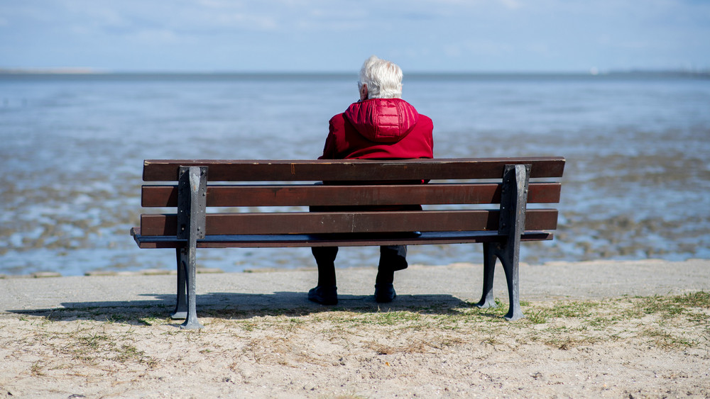 Ein älterer Mann sitzt auf einer Bank und schaut aufs Meer.